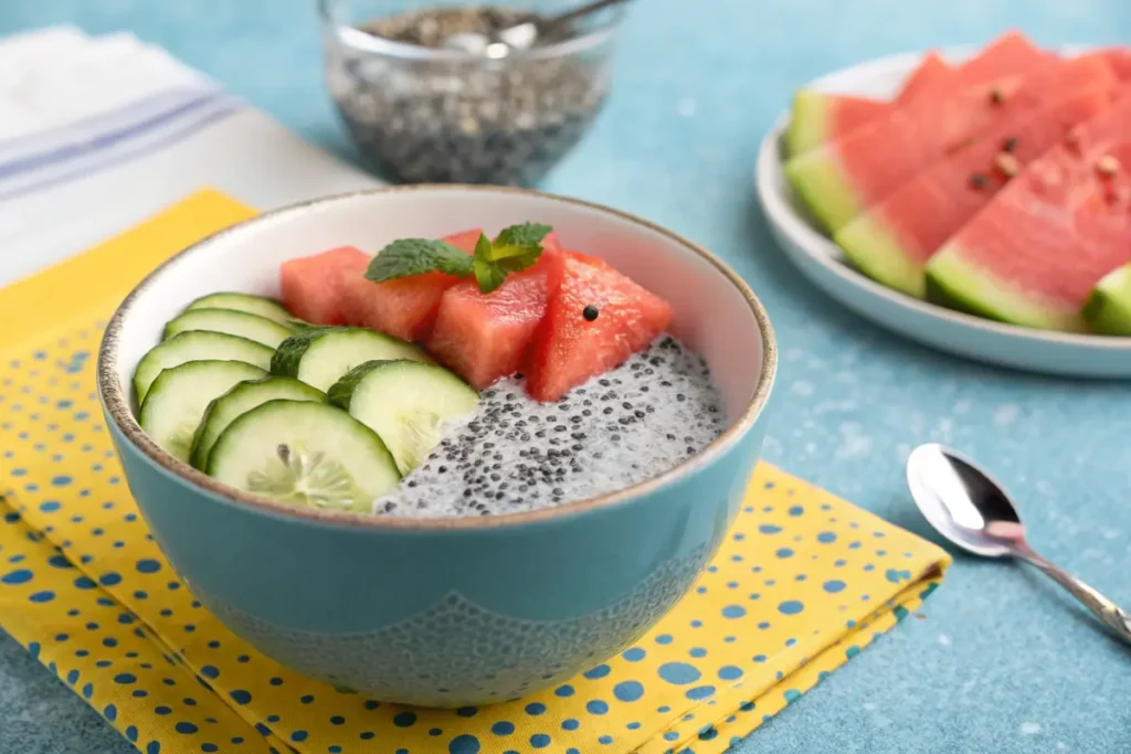 A bowl of chia seed pudding topped with sliced cucumbers, watermelon, and a sprig of mint.