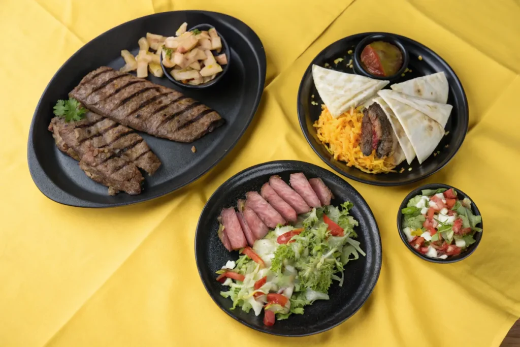 Three plates of food on a yellow tablecloth show grilled skirt beef